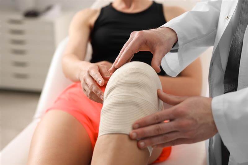 Doctor putting bandage on injured knee o f patient.