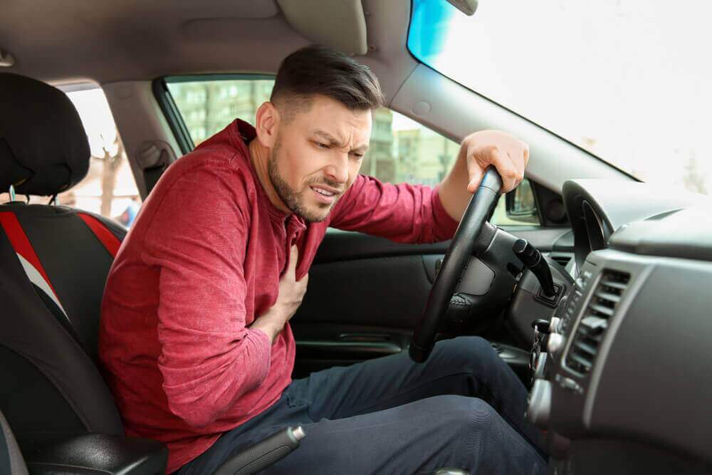 Driver suffering chest pain holding it tight.