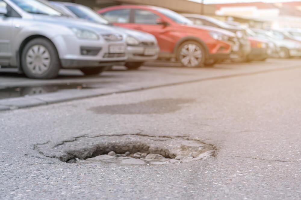 Big pothole with water after rain on asphalt road with car parking lot.