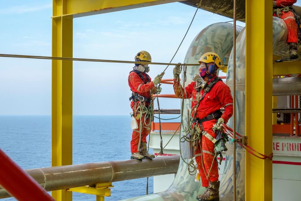 A group of abseilers wearing red coverall and Personal Protective Equipment (PPE) standing on the piepeline managing their rope access with background open sea.